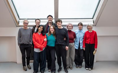 The cast and crew of Guess How Much I Love You stand below a sky light in a blank, white rehearsal room
